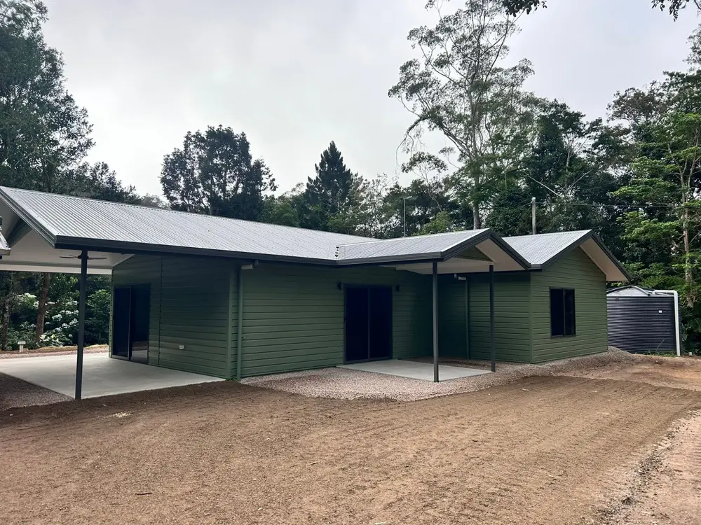 Completed single-storey home with dark green exterior, covered carport and gravel driveway