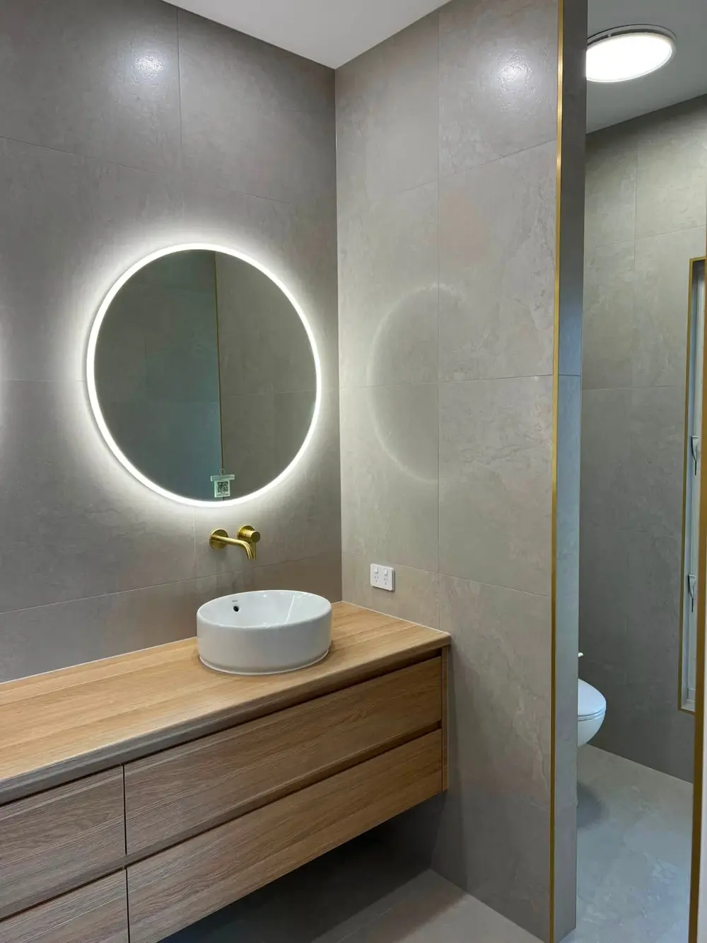 Finished bathroom vanity with illuminated round mirror and timber cabinetry